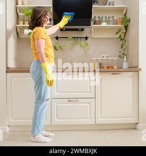 Una donna lava il cappuccio nella sua cucina di casa con uno straccio. Le mani femminili indossano guanti gialli durante la pulizia della cucina Foto Stock