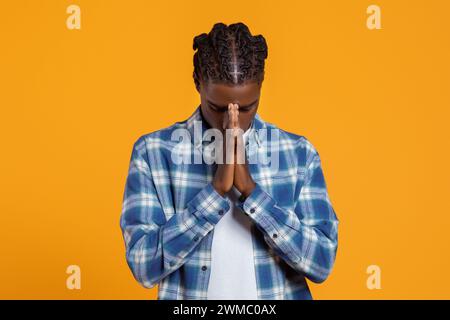 Tranquillo giovane nero in camicia a quadri che prega a occhi chiusi Foto Stock
