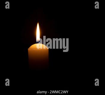 La fiamma o la luce di una singola candela brucia si accende su una grande candela bianca su sfondo nero o scuro sul tavolo della chiesa per Natale, funerale o memoriale Foto Stock