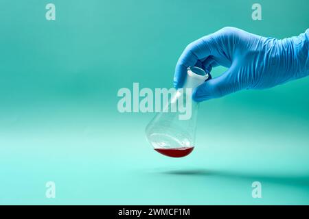 Mano di un medico anonimo in un guanto in lattice contenente matraccio conico con campione chimico rosso in laboratorio durante il test diagnostico Foto Stock