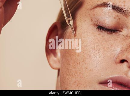 Primo piano di una pelle femminile molto dettagliata con lentiggini e pipetta con siero. Foto ritagliata di una giovane donna con una pelle liscia e perfetta che applica liqui Foto Stock