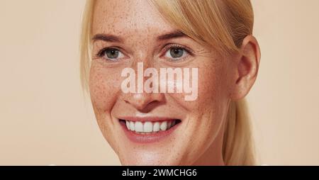 Primo piano dettagliato di una donna sorridente con lentiggini. Giovane donna allegra con capelli biondi su sfondo pastello. Foto Stock