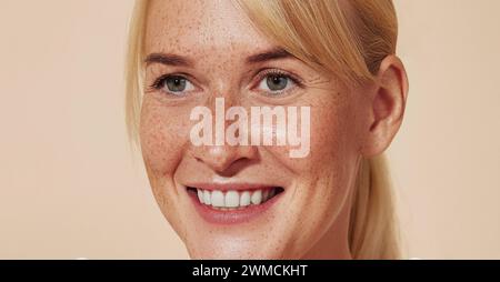 Primo piano dettagliato di una donna sorridente con lentiggini. Giovane donna allegra con capelli biondi su sfondo pastello. Primo piano dettagliato p Foto Stock