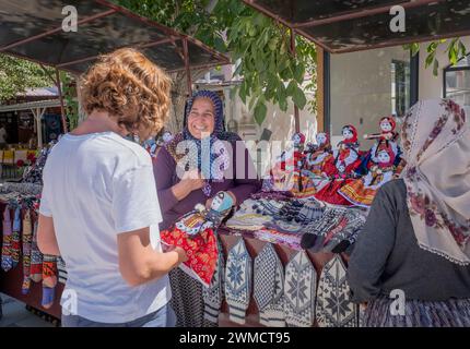 un turista acquista una bambola di stracci fatta a mano vestita con i tipici abiti della cappadocia da una donna turca che fa affari con lei con un sorriso, orizzontale Foto Stock