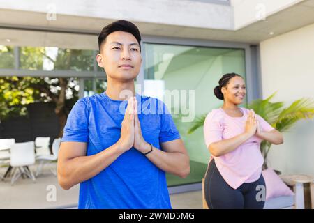 Il giovane uomo asiatico e la donna birazziale praticano yoga all'aperto Foto Stock