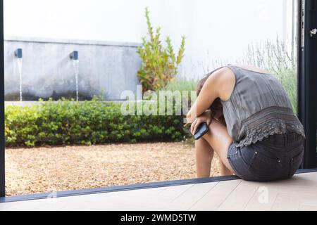 Una giovane donna birazziale sembra angosciata a casa, tenendo in mano uno smartphone Foto Stock