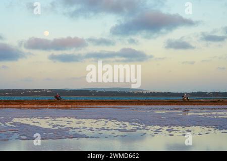 Moto che attraversano le saline al tramonto con luna piena nei pressi di Estany Pudent (la Savina, Parco naturale di Ses Salines, Formentera, Isole Baleari, Spagna) Foto Stock