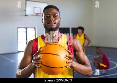 Uomo afroamericano che tiene una pallacanestro in una palestra Foto Stock