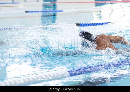 Un giovane nuotatore maschile birazziale nuota in una piscina coperta Foto Stock