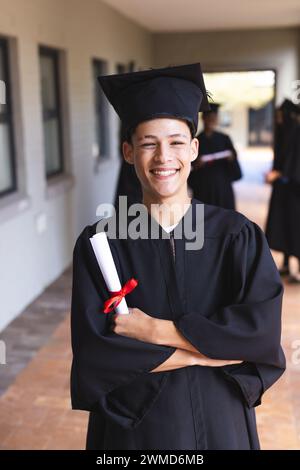 Fiero ragazzo birazziale adolescente in abito da laurea Foto Stock