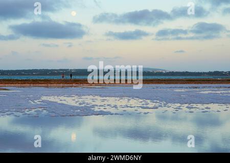 Camminatori che attraversano al tramonto con la luna piena le salinas vicino a Estany Pudent (la Savina, Parco naturale di Ses Salines, Formentera, Isole Baleari, Spagna) Foto Stock