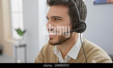 Bell'uomo ispanico con barba che indossa le cuffie in un moderno interno dell'ufficio Foto Stock