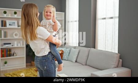 Madre allegra che tiene in braccio la figlia sorridente, in piedi nella loro accogliente casa Foto Stock