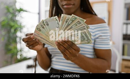 Donna africana che tiene i dirham in casa, ritrae la finanza in un ufficio con chiarezza e attenzione alla valuta. Foto Stock