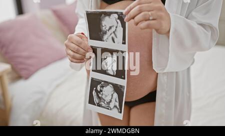 Donna ispanica incinta che tiene in mano immagini ecografiche, in piedi in camera da letto, simboleggia la gravidanza, la maternità e l'anticipazione. Foto Stock