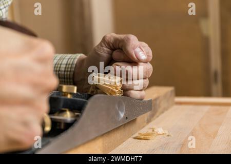 Foto orizzontale afferrando saldamente un piano manuale, un artigiano rasa i ricci da una tavola di legno, dimostrando precisione e tecnica tradizionale di lavorazione del legno Foto Stock