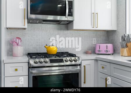 Cucina bianca luminosa con piano cottura in acciaio inox, forno e microonde con arredi colorati Foto Stock