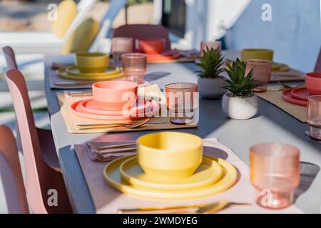 Prepara il tavolo da pranzo all'aperto con ciotole, piatti, bicchieri e argenteria colorate Foto Stock