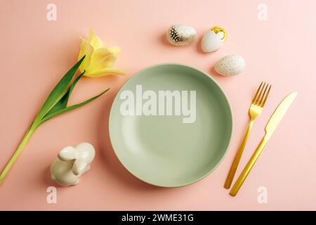 Tavolo con piatto verde, uova di Pasqua, tulipani gialli e coniglietto su sfondo rosa. Vista dall'alto, disposizione piatta. Foto Stock