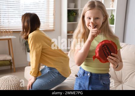 Una bambina divertente con un cuscino che mostra un gesto di silenzio e sua madre a casa. Festa del Fool's Day di aprile Foto Stock