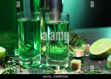 Absinthe in bicchieri da shot, zucchero di canna, rosmarino e lime su tavolo grigio, primo piano. Bevanda alcolica Foto Stock