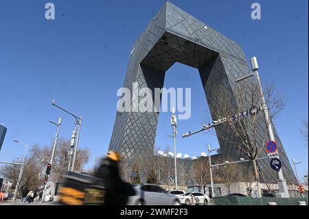 Pechino, Cina. 25 febbraio 2024. Un pilota di e-scooter gira di fronte al quartier generale della televisione di stato cinese CCTV. Credito: Johannes Neudecker/dpa/Alamy Live News Foto Stock