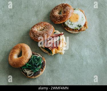 Angolo alto di tre panini per la colazione, bagel tostati impilati con semi di sesamo e ripieni di uova, spinaci e formaggio Foto Stock