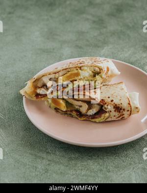 Primo piano di un burrito dimezzato ripieno di fagioli neri, riso, manzo e formaggio su un piatto rosa Foto Stock