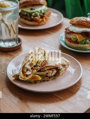 Un piatto diviso con un sandwich a base di bagel, frittelle dolci e frutta su un tavolo di legno Foto Stock