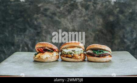 Tre hamburger su un piatto, ognuno con diverse farciture e panini Foto Stock