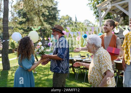 Il nonno regala un regalo avvolto alla nipote come sorpresa alla festa di compleanno. Amici e familiari si riuniscono alla festa in giardino dopo un lungo periodo di distacco Foto Stock