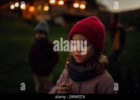 Ritratto di una ragazza carina che soffia la fiamma su un bastoncino in fiamme. La famiglia ha un barbecue in giardino in una sera d'autunno. Foto Stock