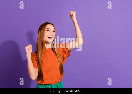 Ritratto della signora in t shirt del famoso marchio di abbigliamento, ha alzato i pugni per festeggiare gli sconti isolati su sfondo di colore viola Foto Stock