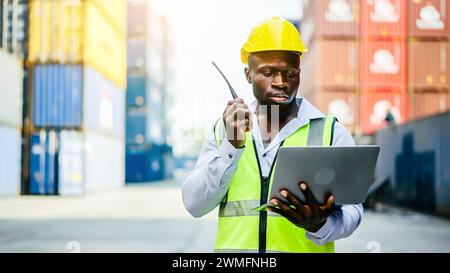 Un capofila con un computer portatile e una radio in piedi davanti ai container di carico Foto Stock