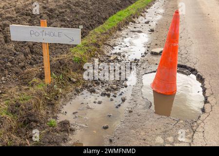 Pozzo, profondo pozzo pieno di acqua piovana, con cono stradale e cartello a sinistra che indica il pozzo sulla strada rurale a binario unico nell'East Yorksh Foto Stock