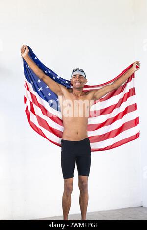 Il giovane nuotatore maschile birazziale celebra la vittoria drappeggiata nella bandiera americana Foto Stock