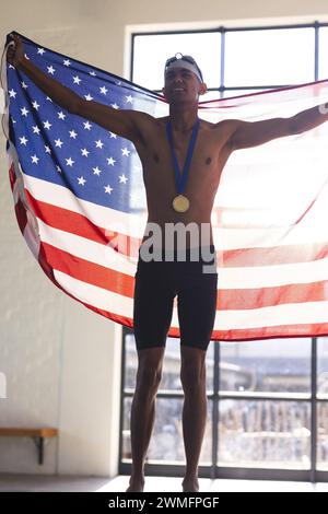 Il giovane nuotatore maschile birazziale celebra la vittoria con una bandiera americana Foto Stock