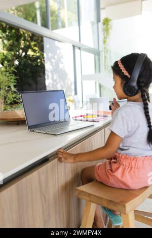 Ragazza birazziale impegnata nell'apprendimento online a casa utilizzando un notebook Foto Stock