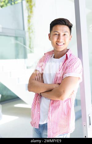 Il giovane uomo asiatico si trova con fiducia in un luminoso ambiente d'ufficio Foto Stock