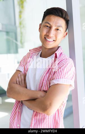 Il giovane uomo asiatico sorride con fiducia in un luminoso ambiente d'ufficio Foto Stock