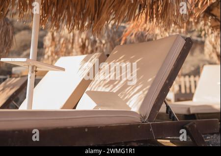 Primo piano di sedie a sdraio con ombrelloni di paglia sotto il sole caldo Foto Stock