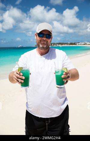 Happy Bearded Man tiene due drink tropicali sulla spiaggia dei Caraibi Foto Stock