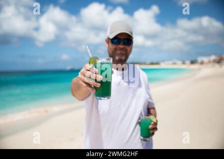 Happy Millennial Man sorseggia un drink tropicale sulla spiaggia dei Caraibi Foto Stock