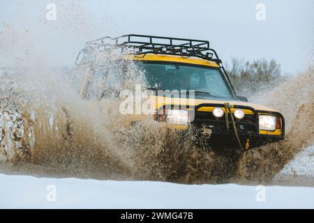 Un SUV spruzza fango durante la guida attraverso una pozzanghera in inverno. Foto Stock