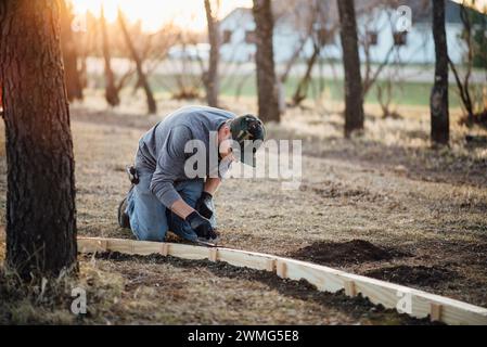 Ampia vista frontale dell'uomo che si inginocchia durante il lavoro manuale nel cortile Foto Stock