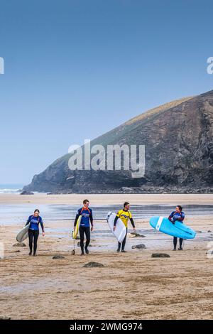 Tre surfisti principianti e il loro istruttore di surf che portano le tavole da surf dopo una lezione di surf al Mawgan Porth in Cornovaglia, nel Regno Unito. Foto Stock