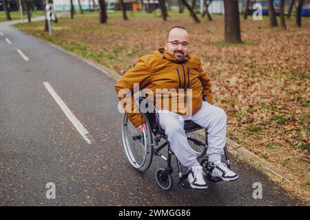 Ritratto di un uomo paraplegico in sedia a rotelle nel parco. Sta rotolando sulla strada. Foto Stock