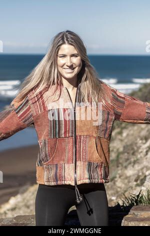 donna bionda che indossa una giacca colorata, davanti a una vista panoramica dell'oceano sotto un cielo limpido Foto Stock