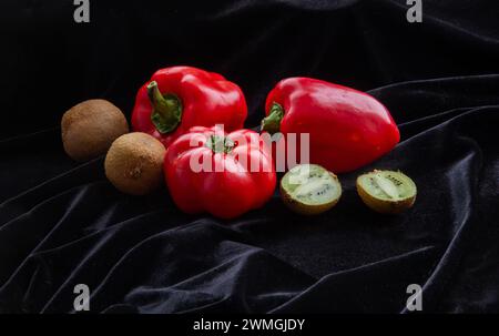 Peperoni e kiwi su tessuto nero. Un taglio di kiwi. La verdura e la frutta sono ricche di vitamina C. mangiare sano in inverno quando piccoli quanti Foto Stock
