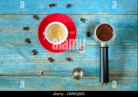 tazza di caffè espresso appena preparato con portafiltro, chicchi di caffè e cucchiaio, piatto, spazio per le copie gratuito Foto Stock